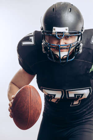 Emotional American football centre forward player in black protective uniform throwing a ball, isolated over white backgroundの写真素材