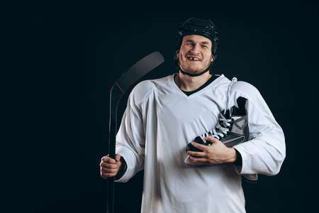 Smiling hockey player looking at camera with skates over shoulder. Isolated on blueの写真素材