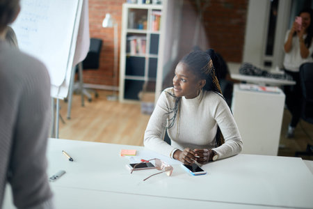 Smiling Young African Businesswoman sitting at the table and listening to the clients offer. close...