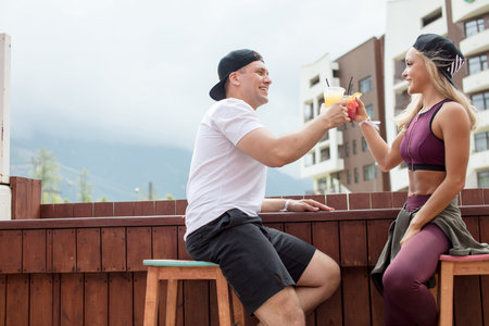 Couple of young athletes relaxing after training in outdoor cafe in charming mountain hotel with...