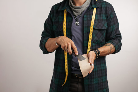 Cropped image of a shoemaker with measure tape and cobbler s tools isolated over grey studio...