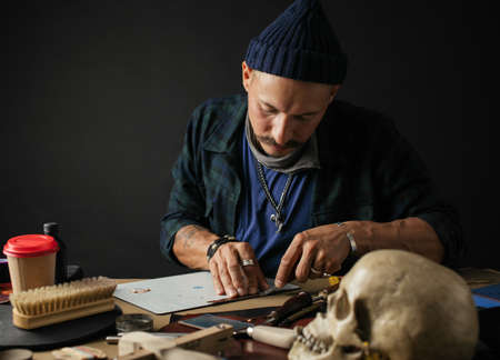 Professional Shoemaker in funny trendy hat is repairing shoes at shoe repair. Shoemaker sews shoes. Footwear artisans and micro-entrepreneurs Conceptの写真素材
