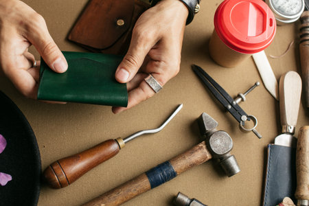 Leather goods master hands and handmade leather wallets lay on table with crafting tools. Workflow...