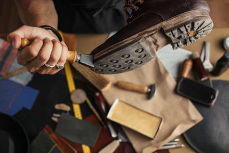Shoemaker hands repairing shoe, close up. Shoemaker peel off sole of a leather boot in a workshop. Fashion custom made shoes.の写真素材