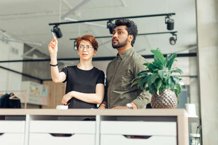 two business partners standing in office building and talking about deals, woman showing coworker his new office placeの写真素材