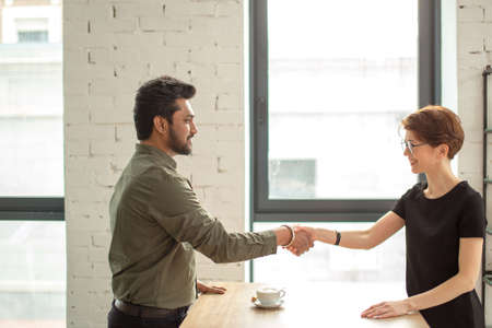 Friendly smiling businessman and businesswoman handshaking in modern officeの写真素材