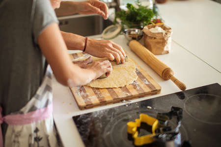 A mother and her little daughter preparing pastry in the kitchen. Little girl using metallic form to cut the dough. Homemade baking and cooking, close up.の写真素材