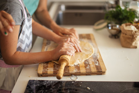 Family business. Female grown up and kid s hands flattening the dough using a rolling pin, close up