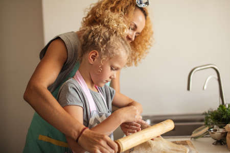 Attractive caucasian mother teaching her curly joyful daughter how to bake cookies for holidays. Easter baking preparation. Easter food concept.の写真素材