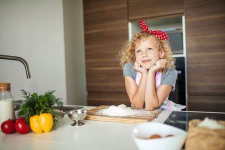 Little pretty female cutie with red headband in apron dreaming while learning to make pastry dough for Christmas cake.の写真素材