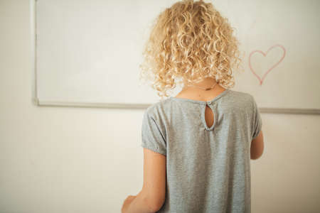 Schoolgirl in home wear writing something on white board on the wall with a marker, rear view. Learning and school concept.の写真素材