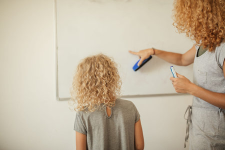 Rear view of blonde curly haired woman drawing on white board with her little daughter. concept....