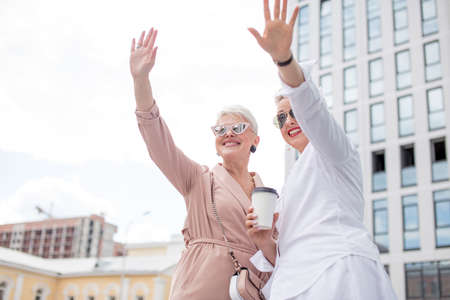 Happy businesswomen with coffee cup conversing outside office buildingの写真素材