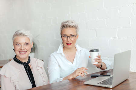 Two business woman discussing work in cafe. Freelancers are generating ideas by using laptopの写真素材