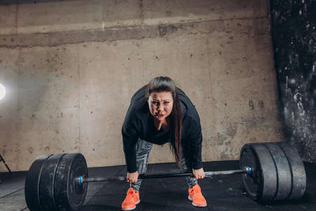angry crazy plump sportswoman holding barbell and looking at the camera. full length photo. effort in lifting weightの写真素材