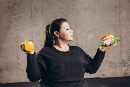 Obese man holding dumbbell eating burger, refusing from doing sport, addiction. close up photoの写真素材