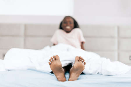 happy cheerful girl lying in the bed and showing her nacked feet. close up photo. funny legsの写真素材
