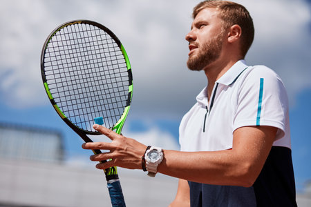Determined blonde male tennis player is ready to return a strong serve, being motivated by a trainer...