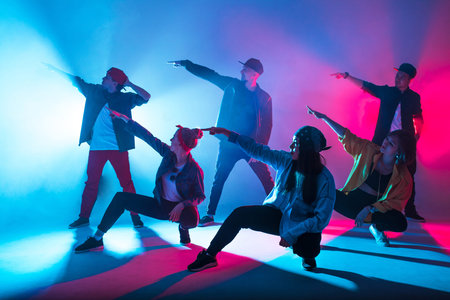 Group of diverse young hip-hop dancers in studio with special lighting effects in blue and pink...