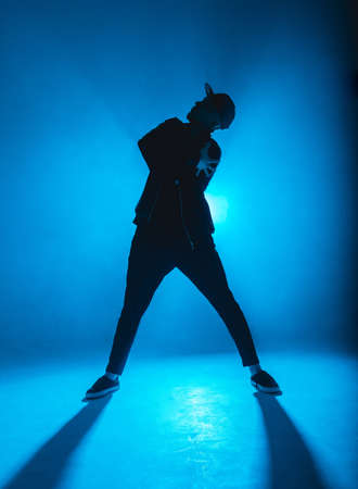 Silhouette of man giving solo performance, dancing alone in hip hop style on club scene with blue neon lightning and smoke.の写真素材
