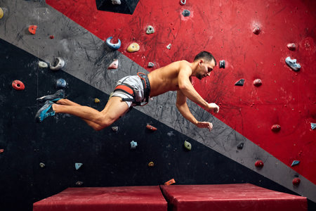 Motion shot of male climber falling on mat from climber wall at an indoor climbing gym.
