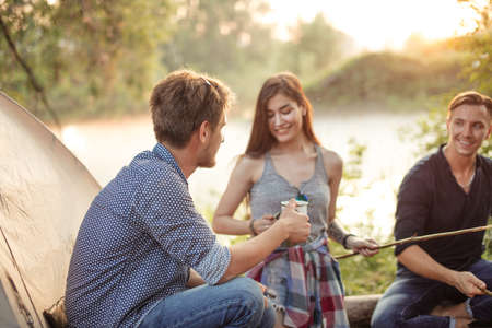 back view photo. young man drinking water in front of friends. forest, river on the background of the photoの写真素材