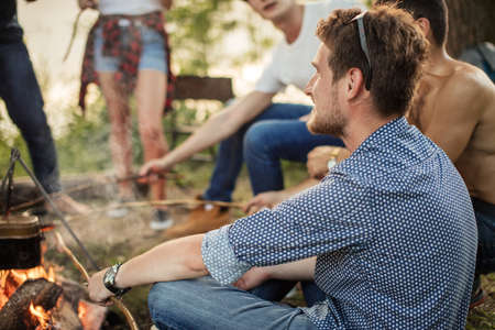thoughtful beaded handsome guy is resting near the bonfire. back view photoの写真素材