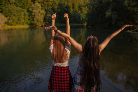 two good looking girls are rejoicing at great breathtaking landscape of park . back view photo. tourists with raised arms enjoying the magnificent view. pleasure conceptの写真素材