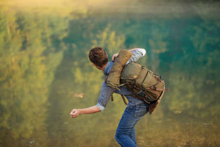 funny tourist is throwing stones in water on a summer day. back view photo. free time. game conceptの写真素材