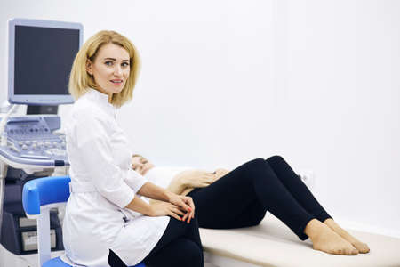 awesome young fair-haired nurse sitting nex to the pregnant woman indoors. close up photo.の写真素材