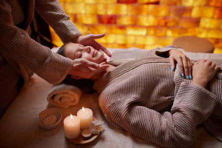 Young girl having massage on her face in spa salon. Wearing bathrobe, candles near her. Beauty treatmentの写真素材