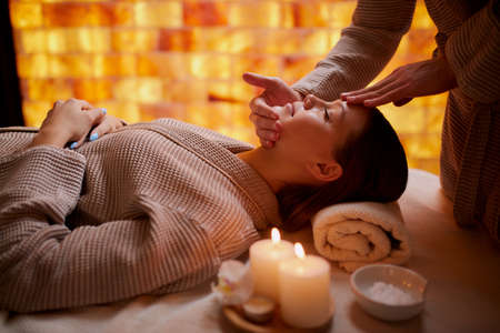 Young caucasian lady get reacreation massage of head, face. Lying down on desk for massages wearing bathrobeの写真素材