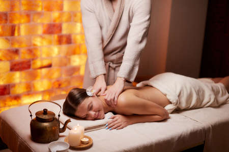 Young lady of caucasian appearance receiving back massage by professonal female hands in spa salon. Leisureの写真素材