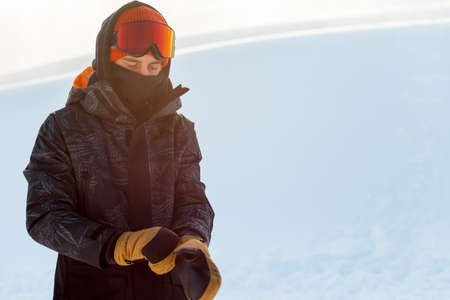 Young snowboarder in sportswear putting on his gloves before snowboarding. copy space. rest. free time. preparationの写真素材