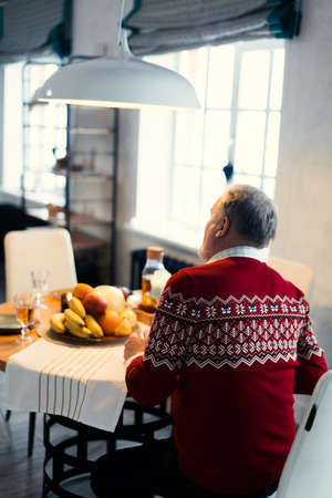 close up back view photo. old man in red sweater having breakfast in the morning.の写真素材