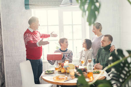 old kind man is congrtulating his large family with event. family exchanges gifts indoorsの写真素材