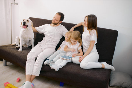 young beautiful family spend time together at home using modern gadgets, tablet. happy family sit on...