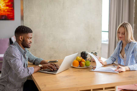 Young multi-ethnic couple sit opposite each other at the kitchen floor, planning their future vacations, make calculations, develop a route. People, vacation, planning conceptの写真素材