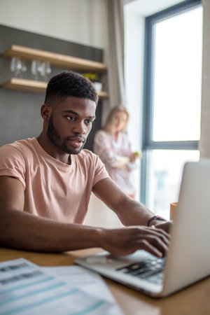 African young businessman working at home in his day-off, making presentation at home with laptop...