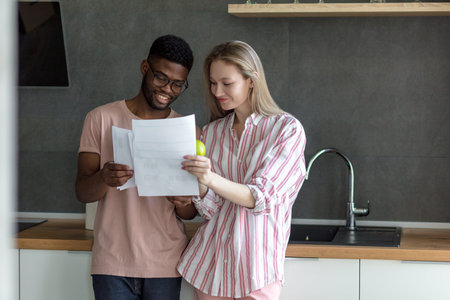 Happy young african husband and his beautiful caucasian blonde wife doing together home budget...