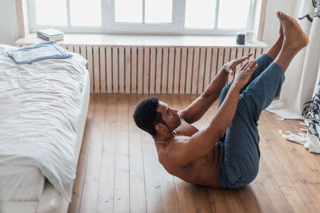 sporty man doing abs workout. ,Training indoors, young attractive muscular man doing morning exercise in the bedrooom, spare time, side view full length photo, interestの写真素材