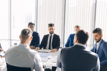 Multiracial male business executives discussing project sitting at conference table in spacious hall...