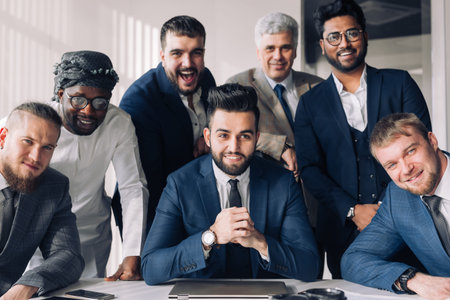 Handsome young bearded caucasian boss in a stylish suit and his cheerful european, indian and...
