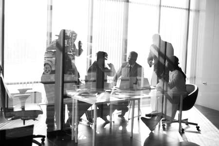 Side view of blurred silhouettes of businessmen talking in conference room, view through the transparent glass wallの写真素材