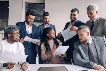 Attractive smiling African business woman gathering paper sheets forms from male company partners greeting each other and expressing regard.の写真素材