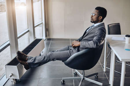 afro-american businessman resting after the conference in his room. full length side view photo. relaxation. free time. man is waiting for his companionsの写真素材