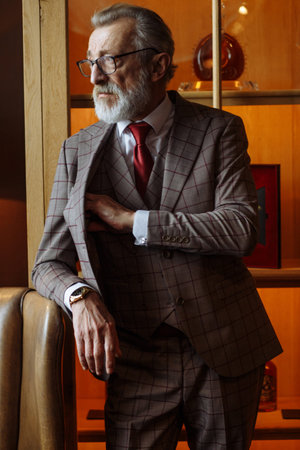 Grey haired old male business owner dressed in formal wear and spectacles, suit with red tie, posing...