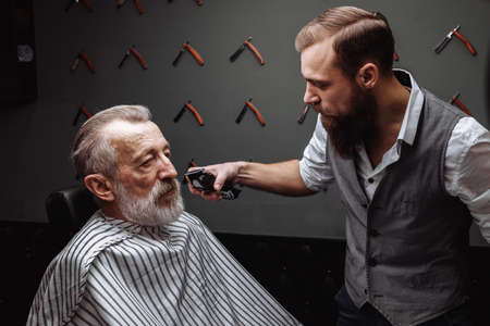 Close up of a hairdresser s work for a handsome respectable old-aged bearded man at the barber shop. He is doing styling with the electric shaver.の写真素材