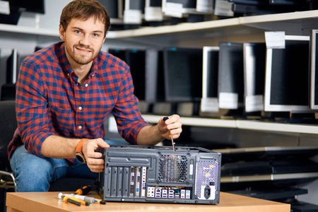happy young bearded man in checked shirt and jeans repairing a PC and looking at the camera. close...