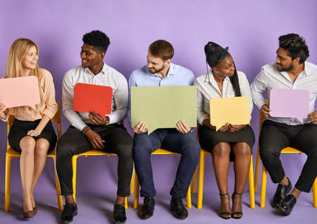 group of young multicultural people sitting and looking at each other with blank thought bubbles waiting for job interviewの写真素材
